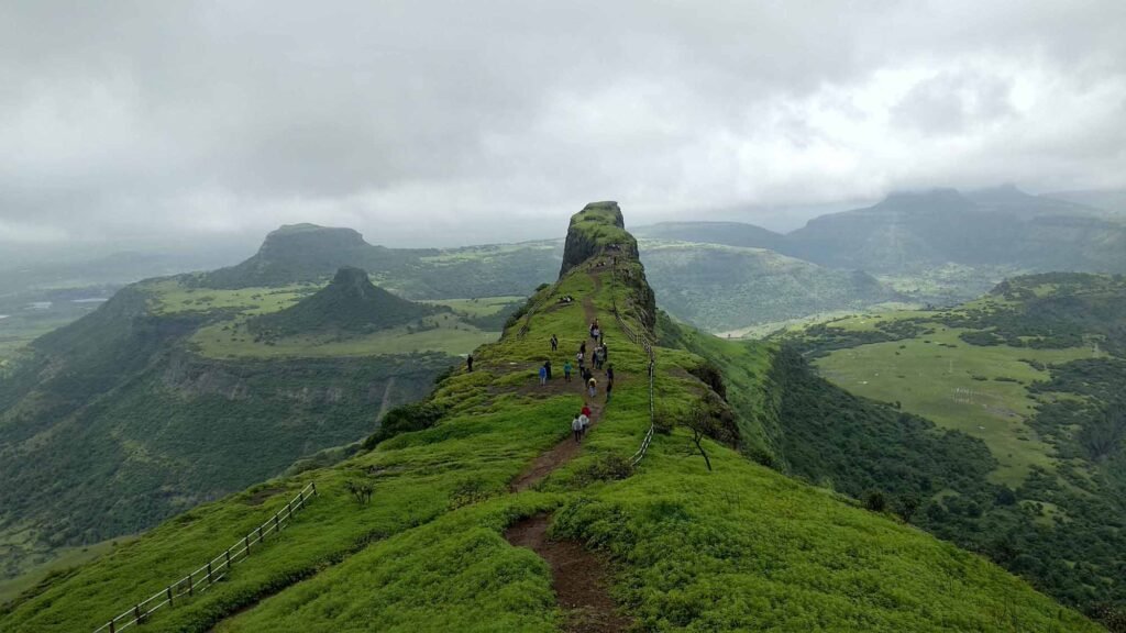 Trekkers walking along the lush green ridge trail to Dhodap Fort surrounded by Sahyadri mountain ranges near Nashik.