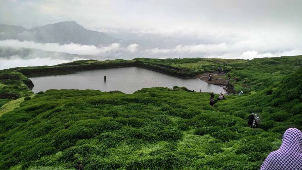Treks Near Nashik showcasing the iconic square-shaped water tank atop Salher Fort surrounded by lush green hills and mist.