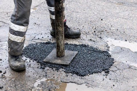 Worker repairing a pothole using compacting tools as part of road maintenance in another city.